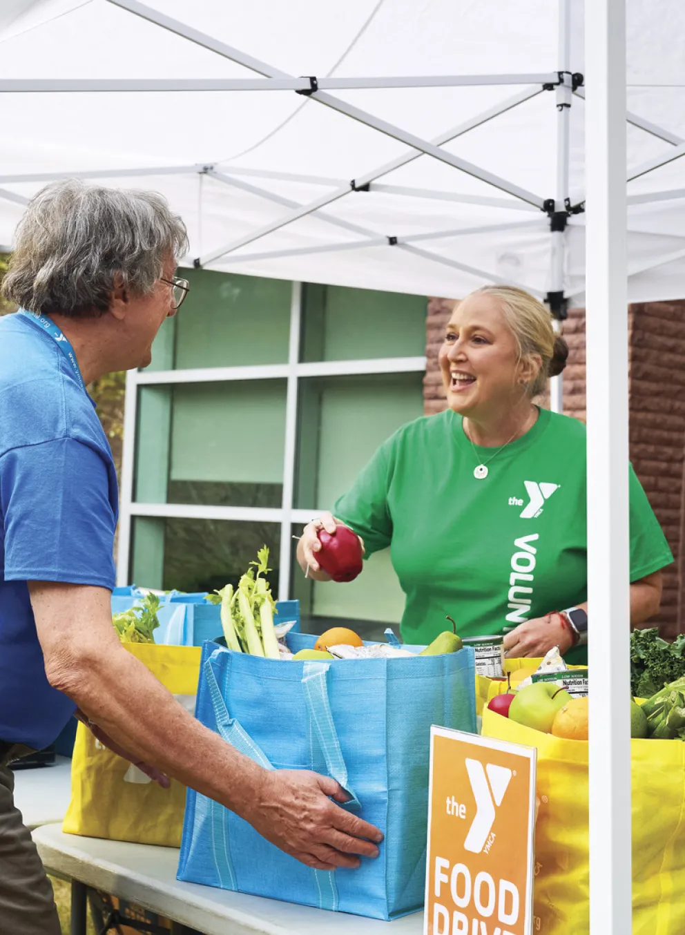 Four adults (some Y staff and some volunteers) work outdoors under a tent at a food drive. Find Your Y